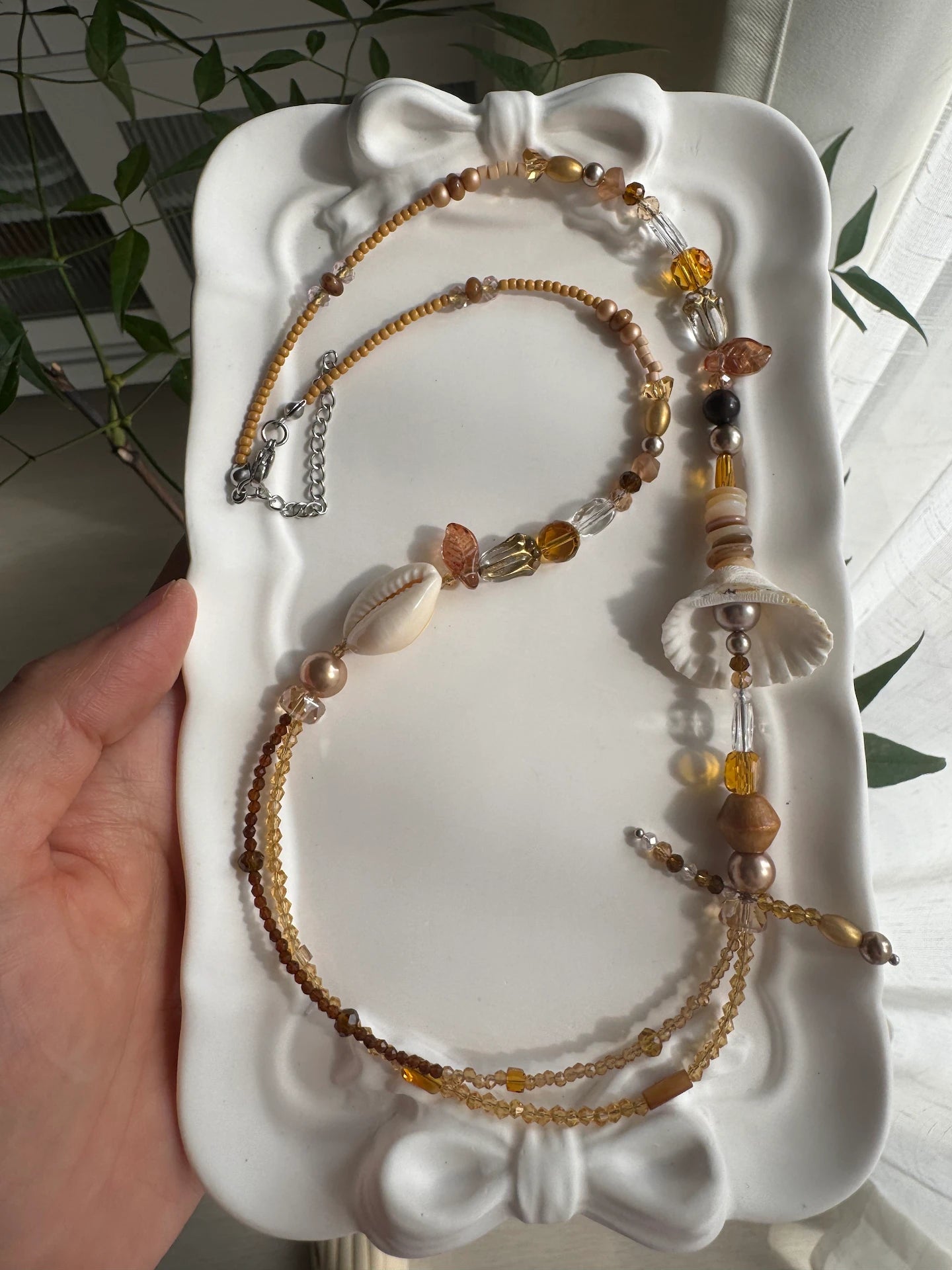 HuibenCraft 1-of-1 vacation-ready bohemian beaded necklace with shimmering coffee-colored beads and organic elements in a white ceramic dish.