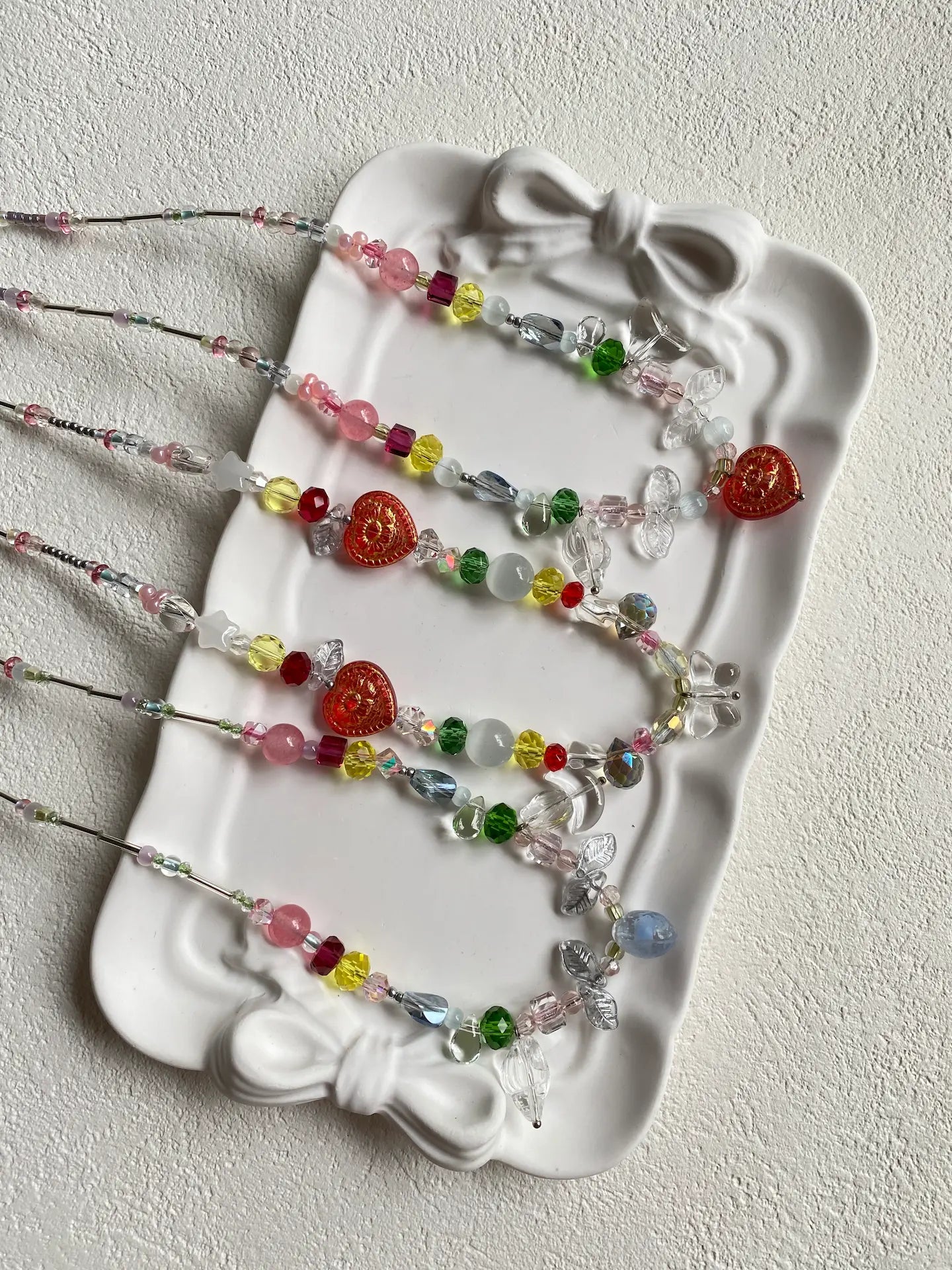Close-up top-down view of three unique HuibenCraft artisan necklaces, showcasing intricate colorful seed beads, a Czech glass lemon, and butterfly pendants.