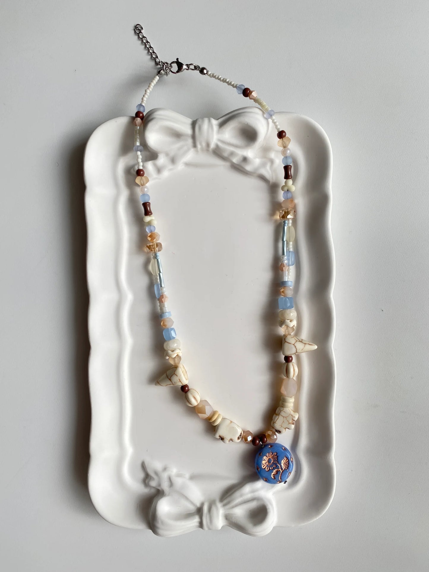 HuibenCraft 1-of-1 vibrant summer vacation necklace with diverse stone shapes and a shimmering blue floral glass pendant in a white ceramic dish.