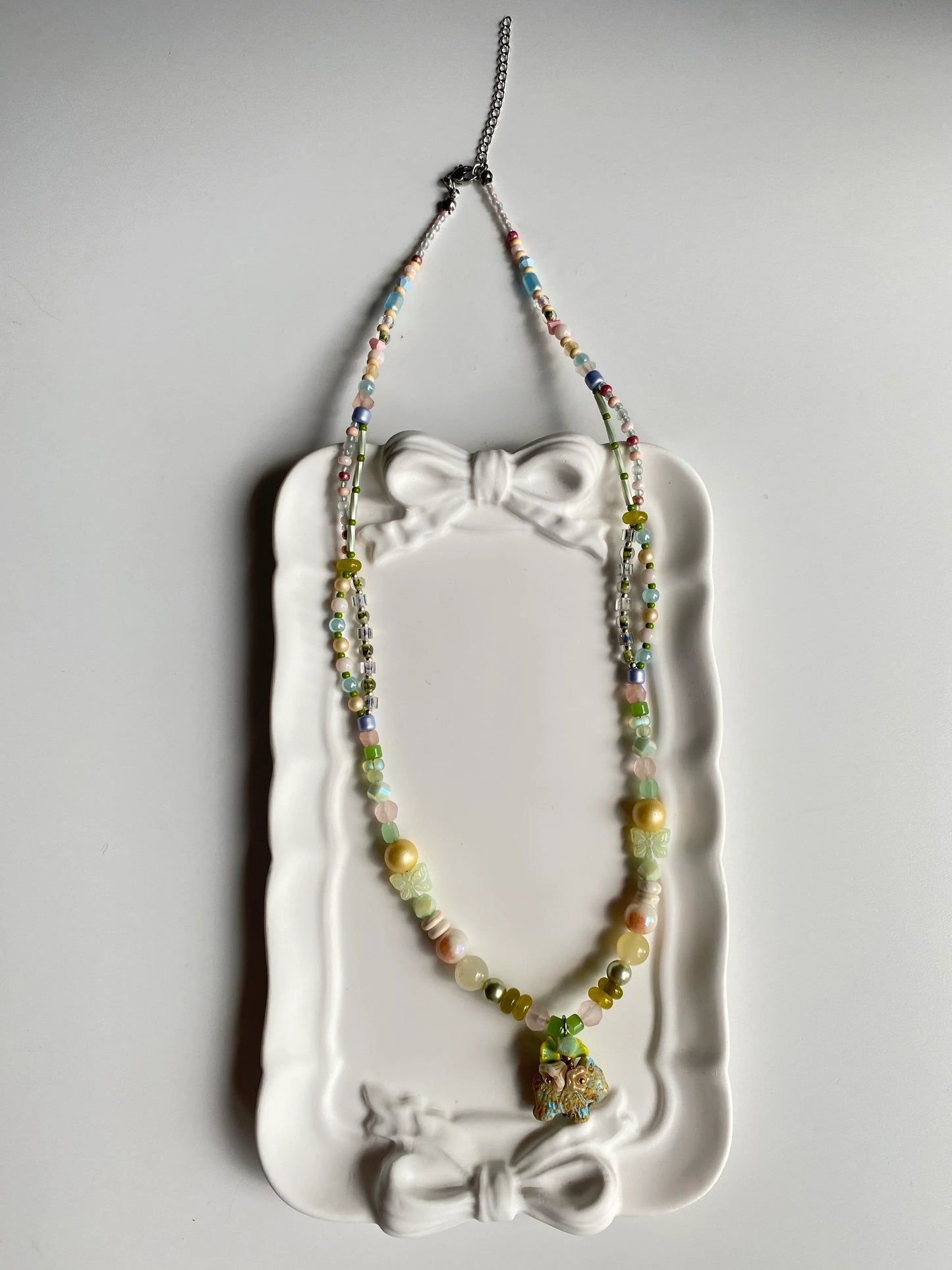 Close-up of a whimsical beaded necklace in a dish, highlighting the bead-woven flower wreath on the Czech glass puppy's back.