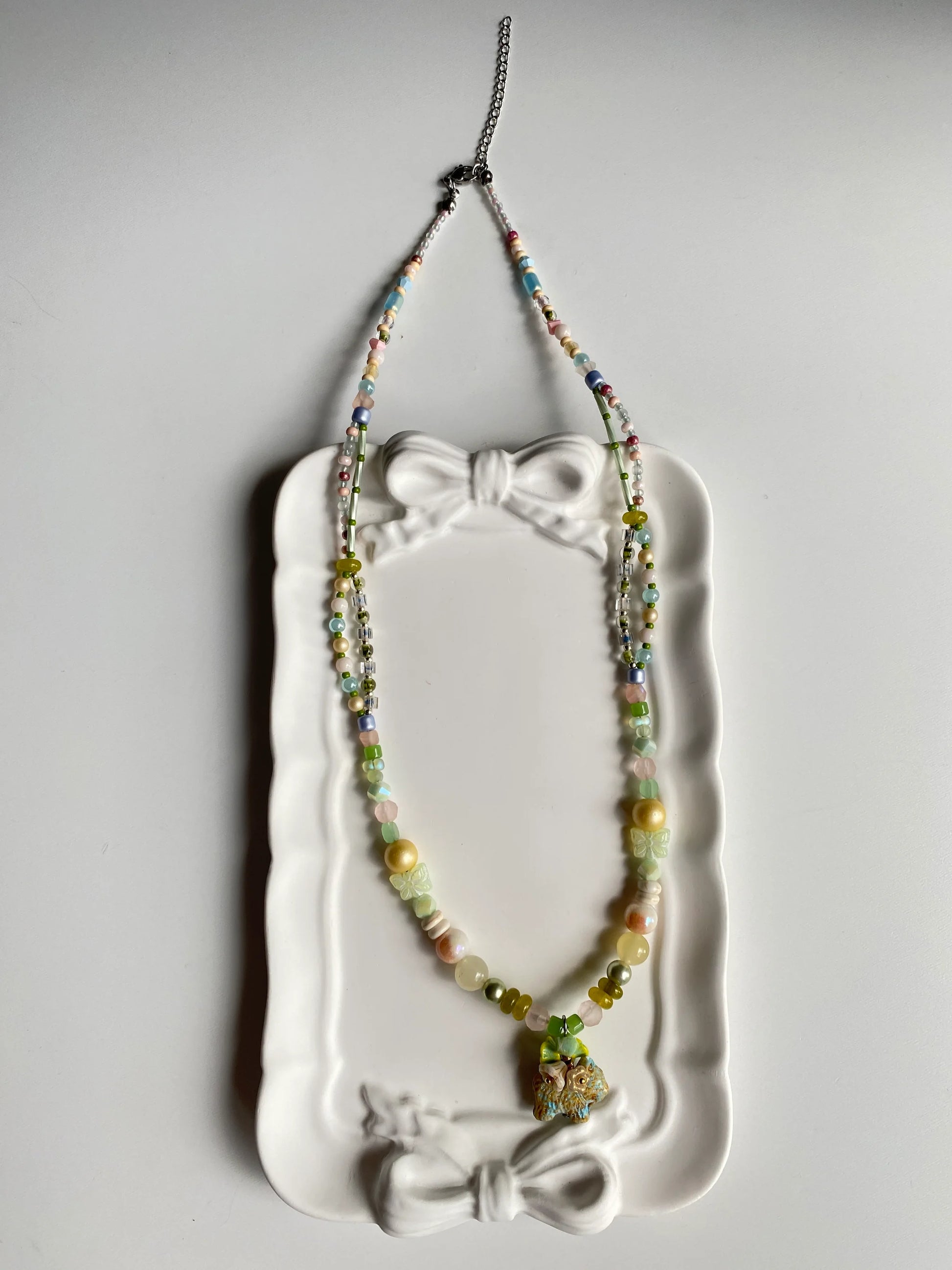 Close-up of a whimsical beaded necklace in a dish, highlighting the bead-woven flower wreath on the Czech glass puppy's back.