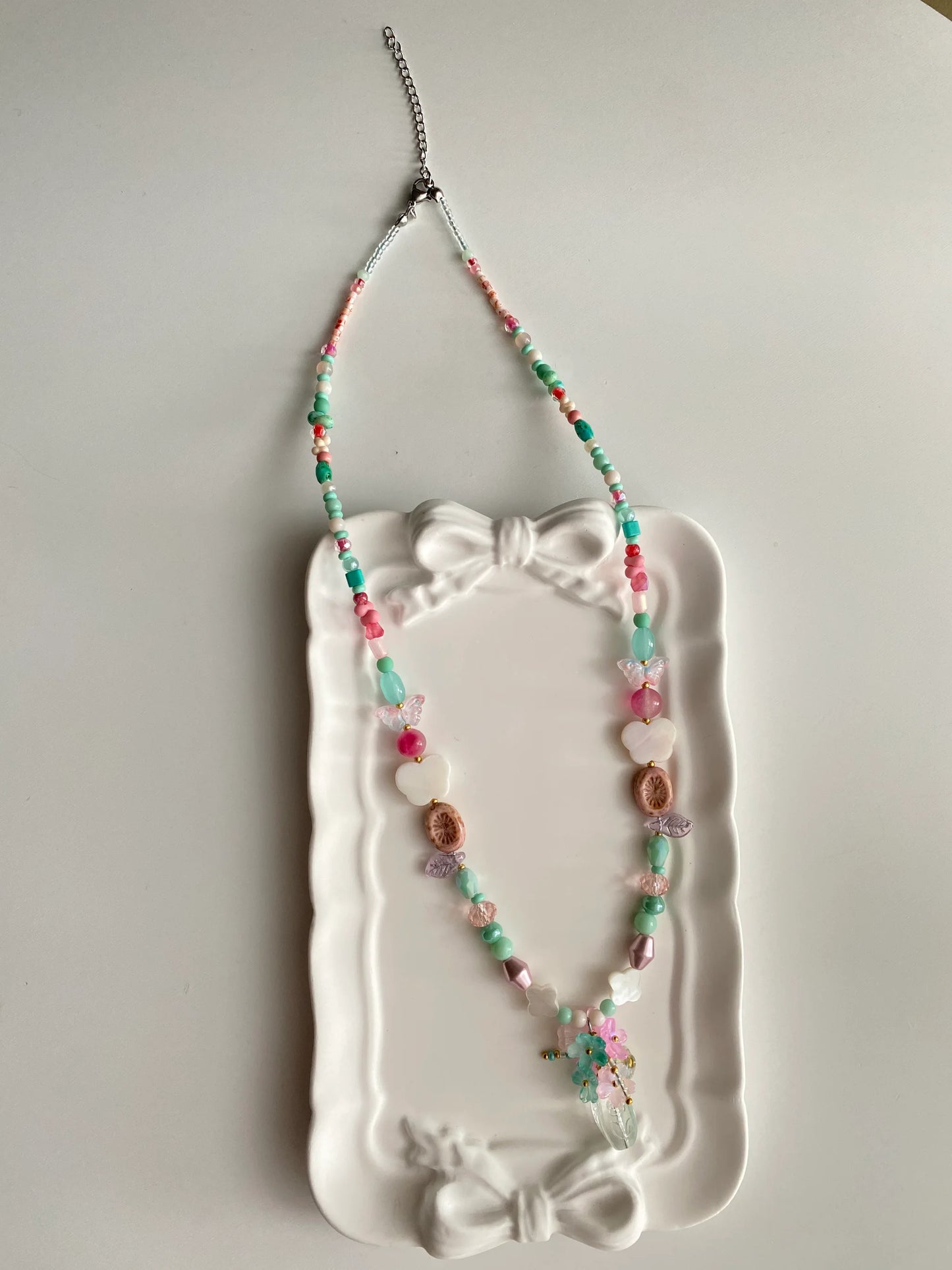 HuibenCraft 1-of-1 whimsical pink floral long necklace with butterfly shell charms and a beaded flower vase in a white ceramic dish.