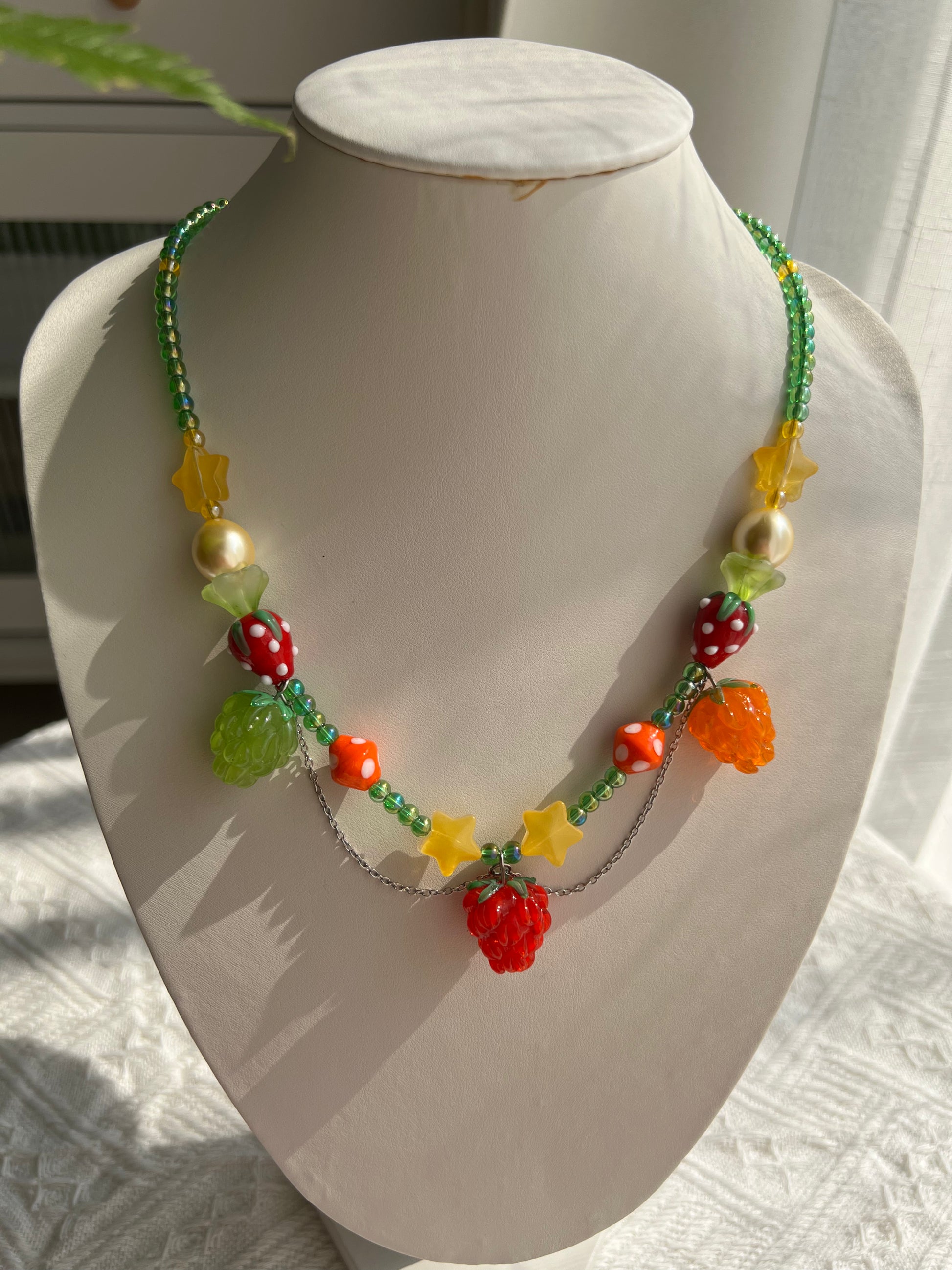 Whimsical Raspberry Strawberry Necklace displayed on a necklace bust, showing its fruit-inspired design.
