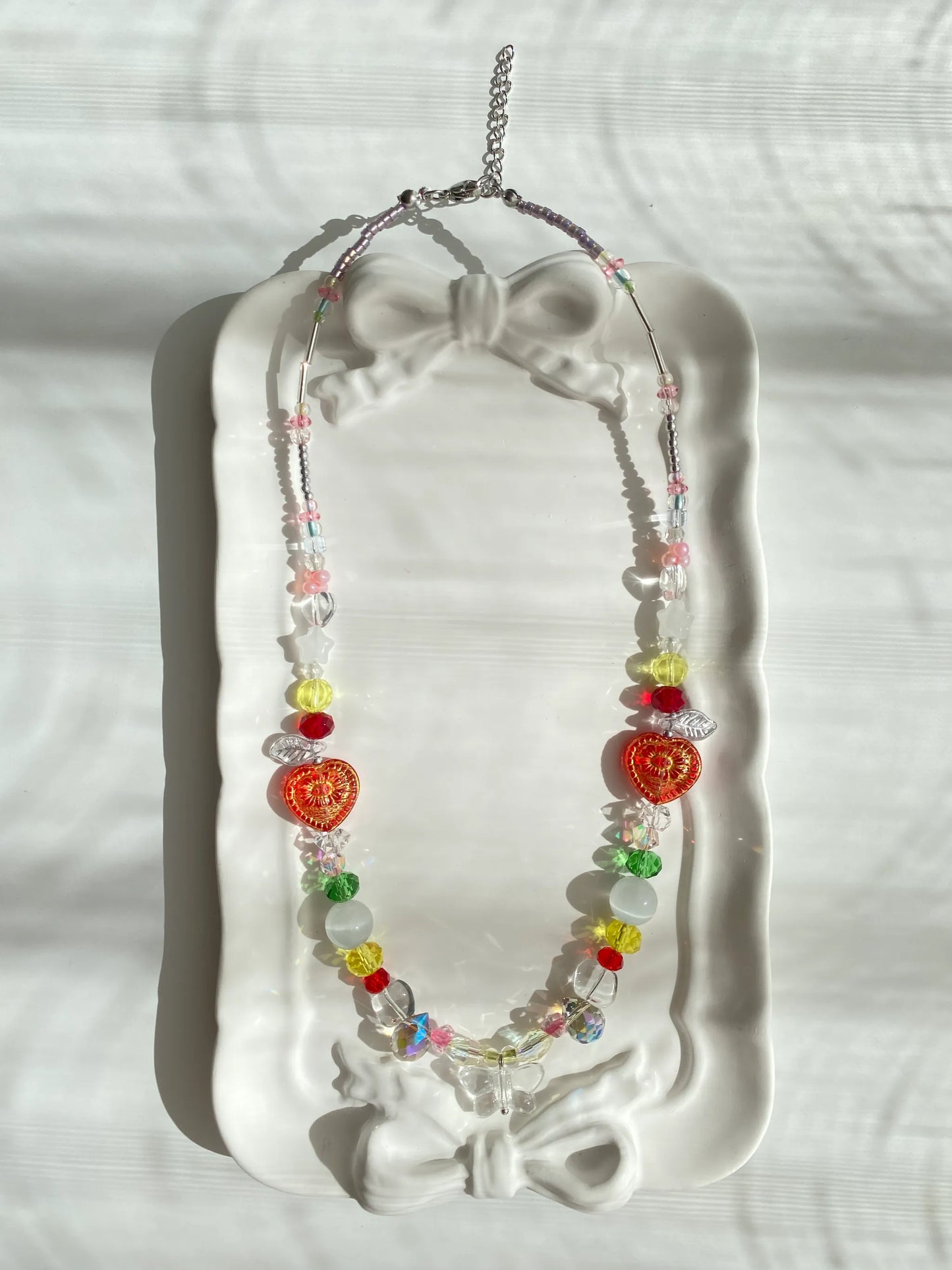 HuibenCraft 1-of-1 brightly colored beaded choker with a clear butterfly pendant and large teardrop accents, elegantly resting inside a sunlit dish.