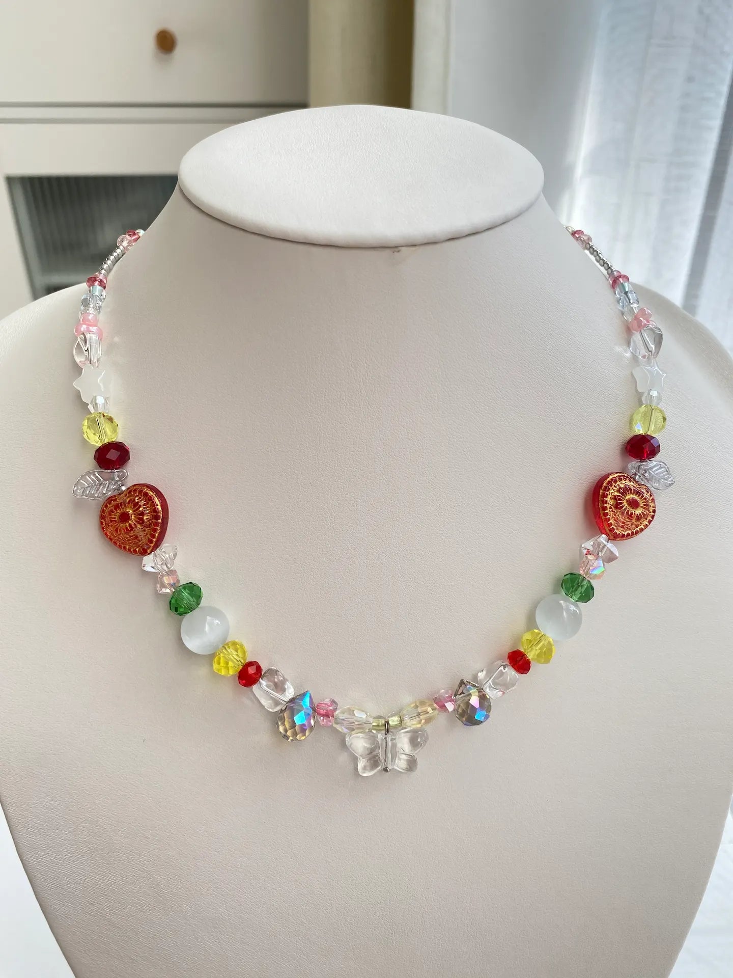 Dazzling HuibenCraft handmade choker featuring a transparent white butterfly pendant and red gold-traced hearts, on a jewelry mannequin in bright sunlight.