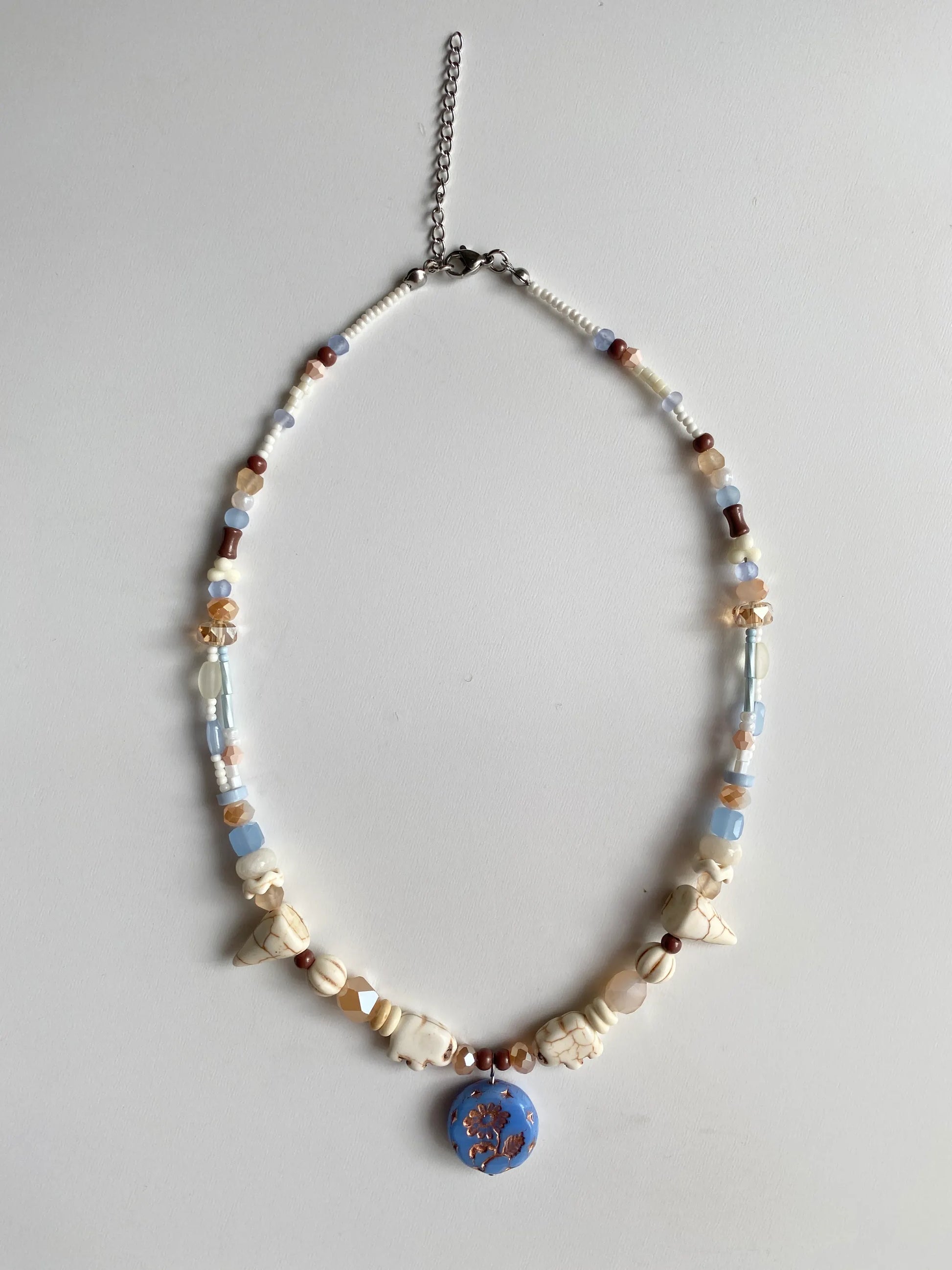 Detailed view of an exotic beaded necklace featuring elephant-shaped white pine stones with natural brown textures and colorful seed beads on a white desk.