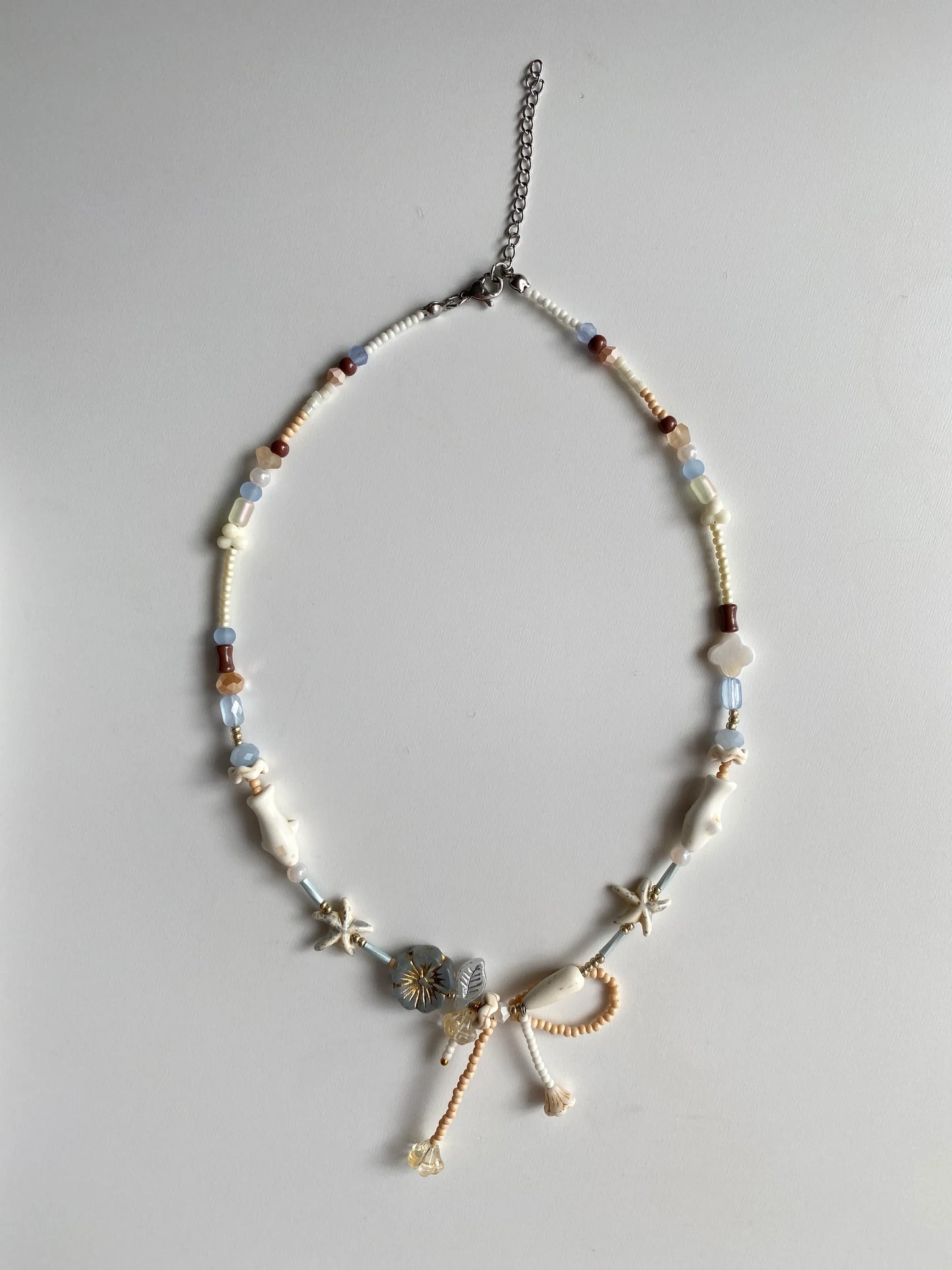 Detailed view of a vacation-style necklace featuring white pine starfish and fish charms, shell clovers, and a delicate bead-woven bow.