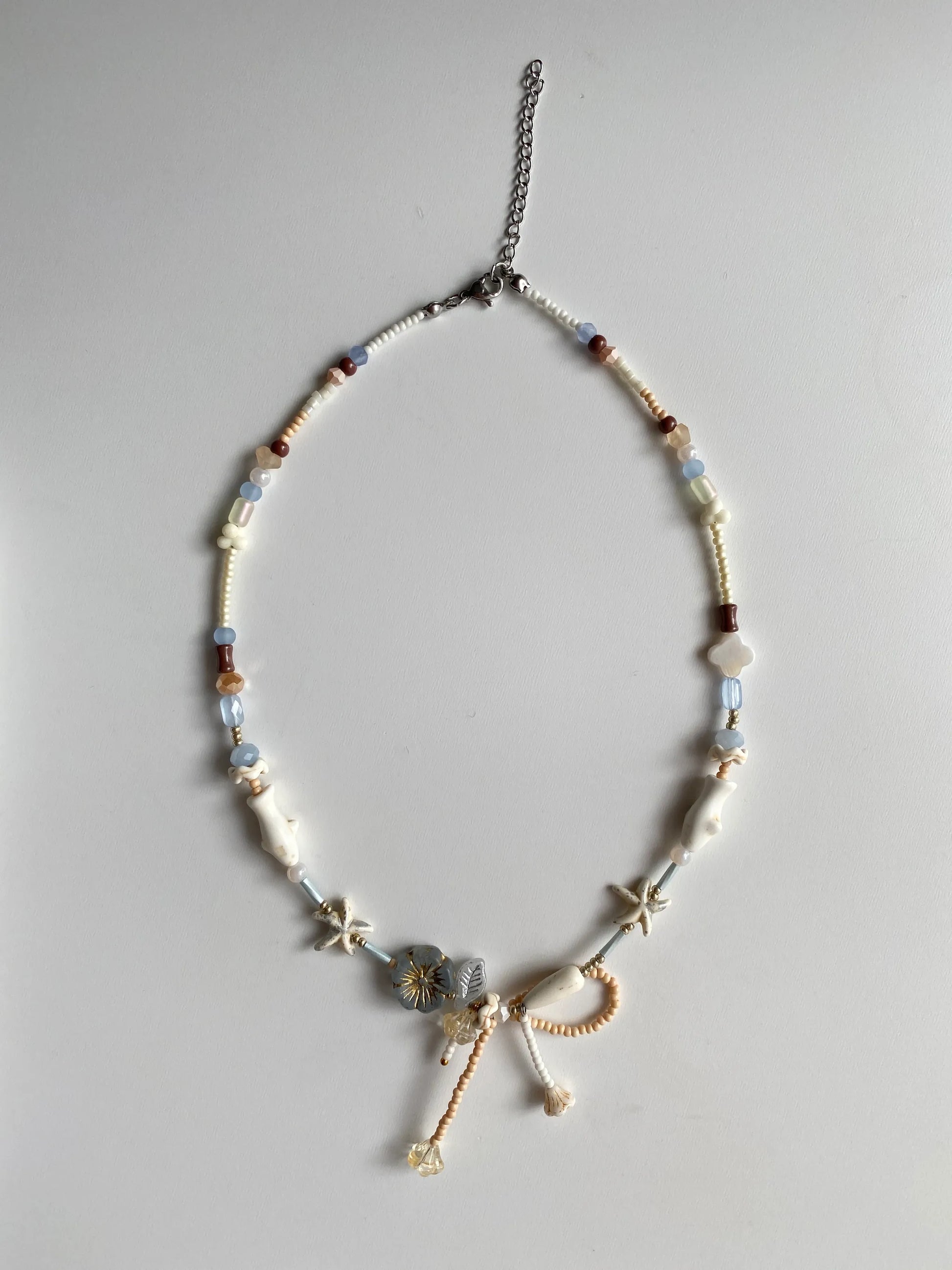 Detailed view of a vacation-style necklace featuring white pine starfish and fish charms, shell clovers, and a delicate bead-woven bow.
